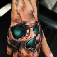 Tatuaje en la mano,  cráneo con ojos de color esmeralda