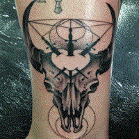 Cult style black ink ankle tattoo of deers skull with swords