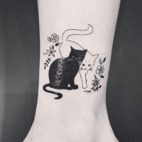 Cute black cat and white cat tattoo on ankle with tiny flowers