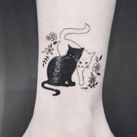 Tatuaje en el tobillo, dos gatos bonitos de colores negro y blanco entre flores diminutos