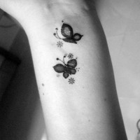 Tatuaje en la muñeca, dos mariposas negras con flores diminutas