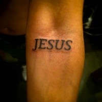 Dark black lettering Jesus religious tattoo on forearm
