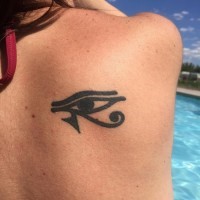 Dark black the Eye of Horus tattoo on lady's shoulder blade in Egyptian style