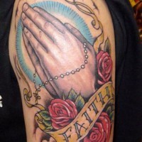 Dramatic style designed colored praying hands with cross flowers and lettering tattoo on shoulder