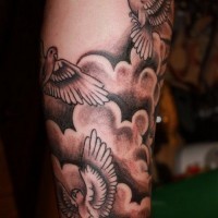 Elegant gray-ink birds flying in clouds tattoo sleeve on forearm