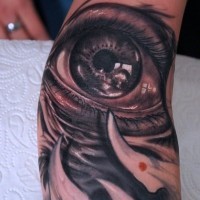 Tatuaje en el brazo, ojo, colmillos, color negro