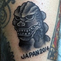 Funny cartoon like black ink Godzilla with lettering tattoo on arm