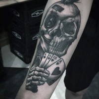 Tatuaje en el antebrazo, mitad cara de Joker  mitad cráneo con naipes, colores negro blanco