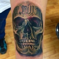 Tatuaje en el antebrazo, cráneo con frase en la frente