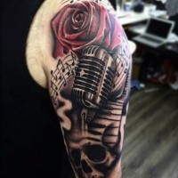 Tatuaje en el brazo,
micrófono, cráneo, rosa roja y notas