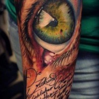 Green eye and inscription tattoo on arm