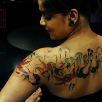 Homemade watercolor like colored upper back tattoo of flowers and dragonfly