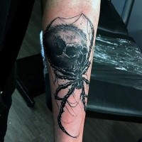Horror style black ink forearm tattoo of spider with human skull