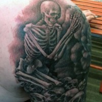 Tatuaje en el hombro, esqueleto terrorífico que ora entre montón de cráneos