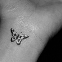 Tatuaje en la muñeca, mariposa diminuta de colores negro y blanco