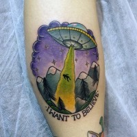 Little cartoon like colorful alien ship with human and lettering tattoo on leg