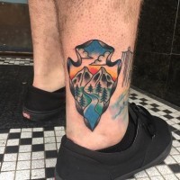 Little cartoon style painted ancient weapon tattoo on ankle stylized with mountains
