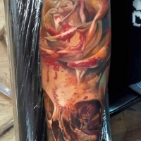 Magnificent multicolored bloody rose tattoo on forearm combined with human skull