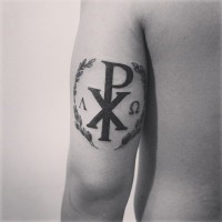 Tatuaje en el brazo, cristograma   Chi Rho  grueso negro y corona de laurel