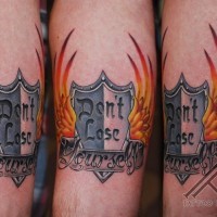 Memorial style colored shield shaped emblem with lettering and flames tattoo on arm