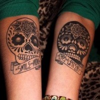 Mexican style different colored little skulls with lettering and flowers tattoo on arm