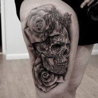 Mexican traditional black and white thigh tattoo of human skull stylized with flowers and lettering
