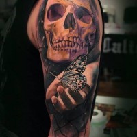 Tatuaje en el brazo,
cráneo grande con mariposa en la mano