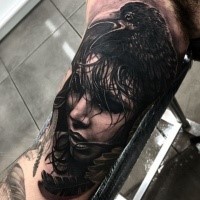 Mystical looking black ink biceps tattoo of sad woman face with crow