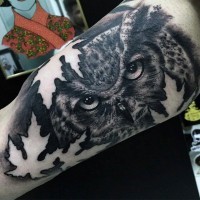 Natürlich aussehende schwarze und weiße Eule Gesicht mit Ahornblättern Tattoo am Arm