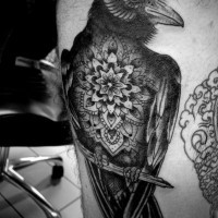 Natural looking black ink crow tattoo on thigh stylized with beautiful flower