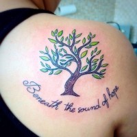 Tatuaje en el hombro, árbol pequeño con hojas verdes i inscripción