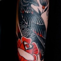 Old school colored little crow tattoo on forearm with cute flowers