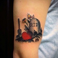 Tatuaje en el brazo, lápida mortuoria con pala corazón y flores, old school