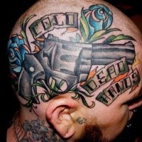 Old school style colored head tattoo of big pistol with flowers and lettering