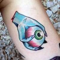 Old school style colored monster hand holding eye tattoo on arm