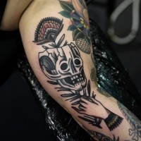 Old school style designed little skull with flower tattoo on arm