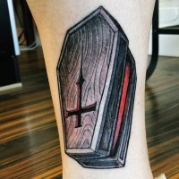 Old style colored wooden open coffin with inverted cross tattoo on leg