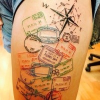 Original colorful thigh tattoo of various stamps and compass