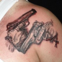 Tatuaje de pistolas con letrero en el hombro