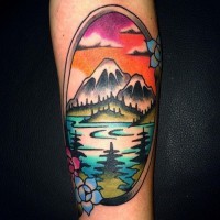 Oval shaped multicolored forearm tattoo of mountain lake with flowers