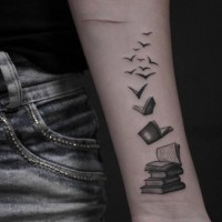 Tatuaje en el antebrazo,  pila de libros con bandada de pájaros