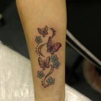 Tatuaje en el antebrazo, bandada de mariposas rosas entre flores diminutas