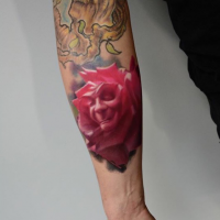 Pink colored forearm tattoo of large rose stylized with face