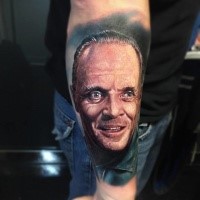 Portrait style colored arm tattoo of Hannibal Lector face