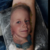 Portrait style colored forearm tattoo of cute looking smiling boy