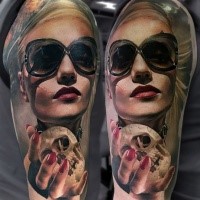 Realism style colored shoulder tattoo of woman with sun glasses and small skull