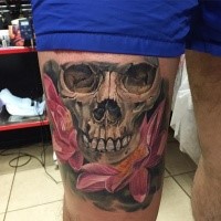 Realism style colored thigh tattoo of human skull with beautiful flowers