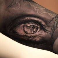 Tatuaje en el brazo, ojo oscuro con cuervos reflejados en pupila