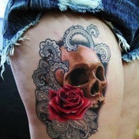 Tatuaje en el muslo, cráneo con rosa en hojas decorativas