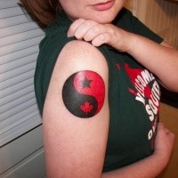 Red and black Asian Yin Yang symbol tattoo on girl's shoulder decorated with maple leaf and star